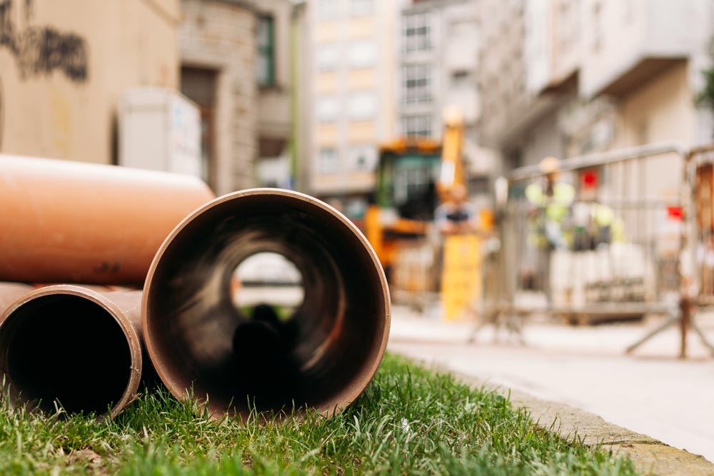 Plaströr ligger i gräset längs en byggarbetsplats